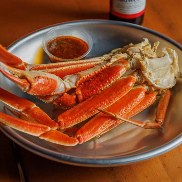 A platter of bright red crab legs and claws with a side of dipping sauce, from Juicy Claws Restaurant.