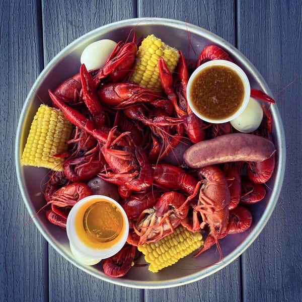 Overhead view of a seafood boil with crawfish, corn, sausage, and dipping sauces in a metal pan.