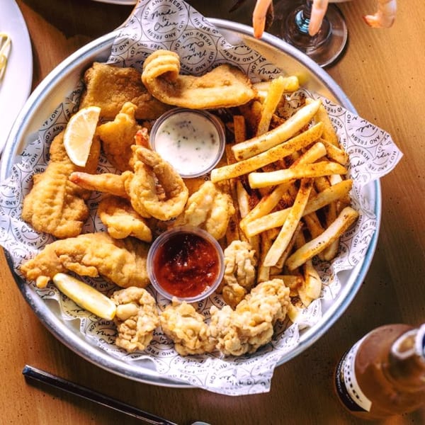 A platter of Juicy Claws fried seafood, fries, and dipping sauces on a wooden table.
