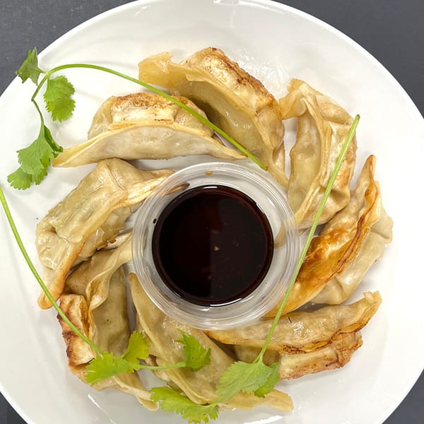 Pan-fried dumplings with a side of soy sauce and cilantro on a white plate.