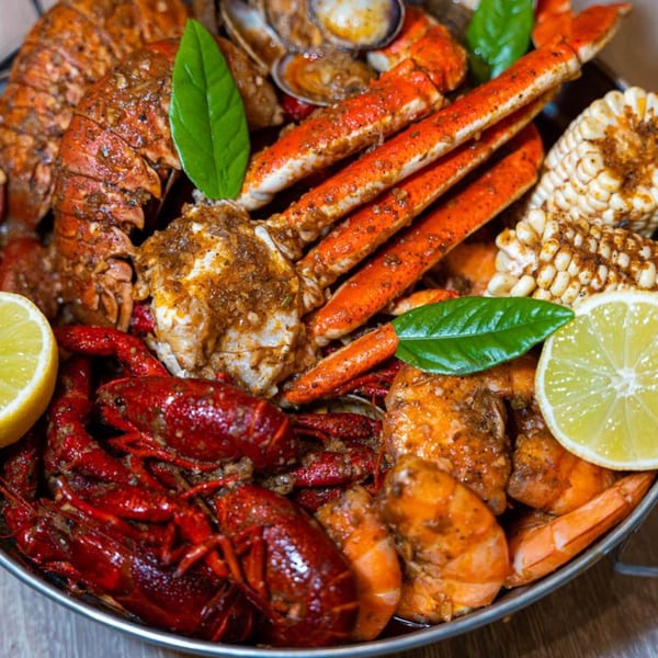 A large platter of Juicy Claws seafood boil with lobster, crab legs, crawfish, shrimp, corn, and lemon.