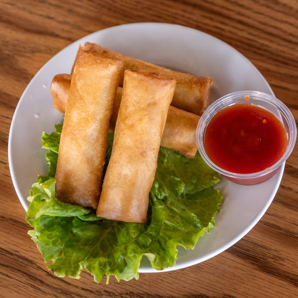 Golden-brown spring rolls on a bed of lettuce with a side of red dipping sauce.