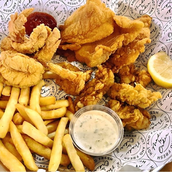 A platter of golden-fried fish, shrimp, and fries with tartar sauce and ketchup.