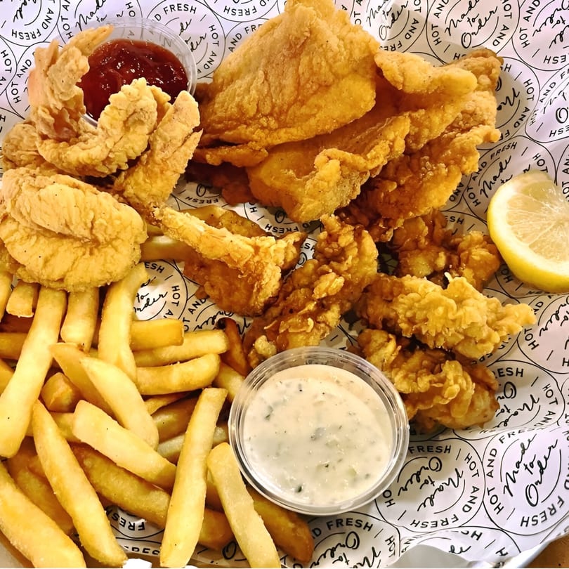 A platter of golden-fried fish, shrimp, and fries with tartar sauce and ketchup.