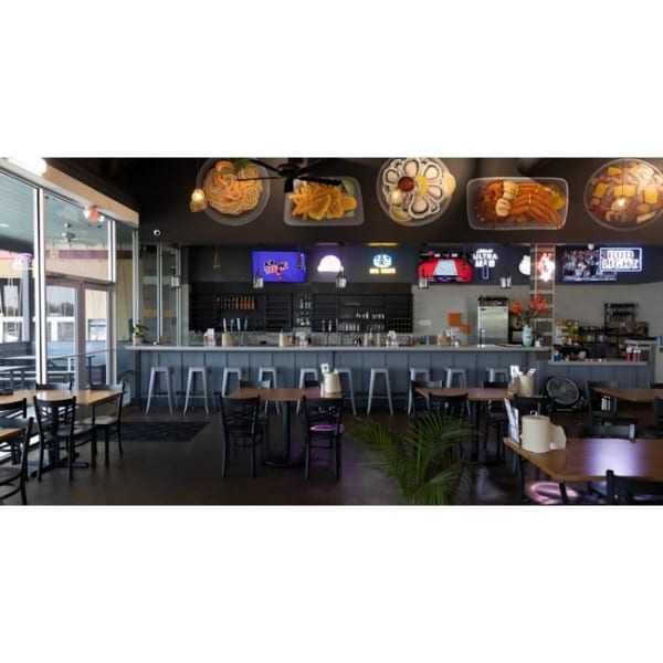 Interior of Juicy Claws Restaurant with a bar, dining tables, and seafood dishes displayed above.