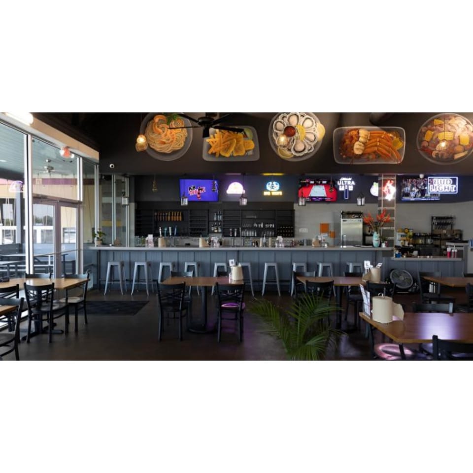 Interior of Juicy Claws Restaurant with a bar, dining tables, and seafood dishes displayed above.