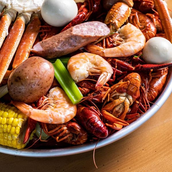 A close-up of a seafood boil with crawfish, shrimp, crab legs, corn, potatoes, sausage, and eggs.