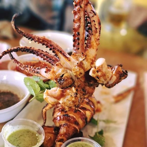 Grilled squid with tentacles, served with green and brown dipping sauces at Juicy Claws Restaurant.