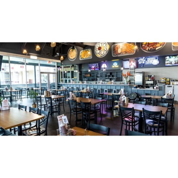 Spacious Juicy Claws Restaurant interior with wooden tables, black chairs, a bar, and large windows.