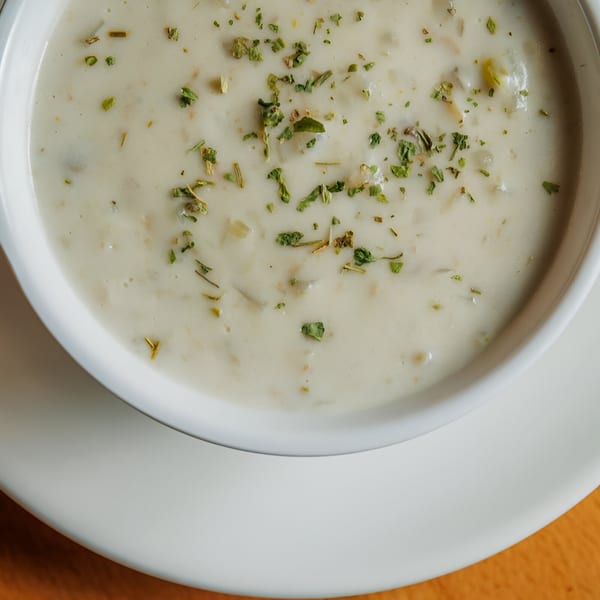 Creamy seafood chowder, garnished with green herbs, served in a white bowl at Juicy Claws Restaurant.