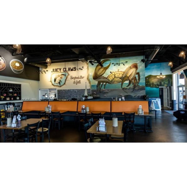 Interior of Juicy Claws Seafood Bar & Grill with crab mural, orange booths, and dining tables.