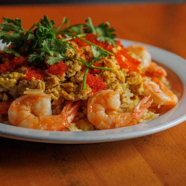 Shrimp fried rice with scrambled eggs, red roe, and fresh cilantro on a white plate.